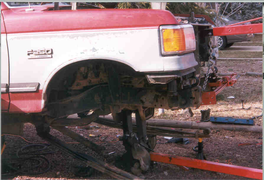 Red and white Ford F-250 front fender removed, truck on jack stands