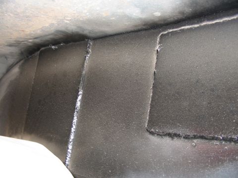 1993 Ford Taurus - Close-up view of a vehicle's undercarriage, revealing welded seams and a dark, textured protective coating.