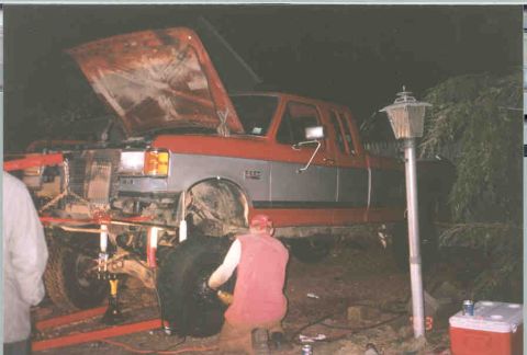 1991 Ford F-250 - Mechanics work on the suspension of a 1991 Ford F-250 truck with its hood up.
