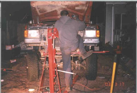 1991 Ford F-250 - Mechanic works on the front end of a 1991 Ford F-250, with the hood raised and engine exposed.