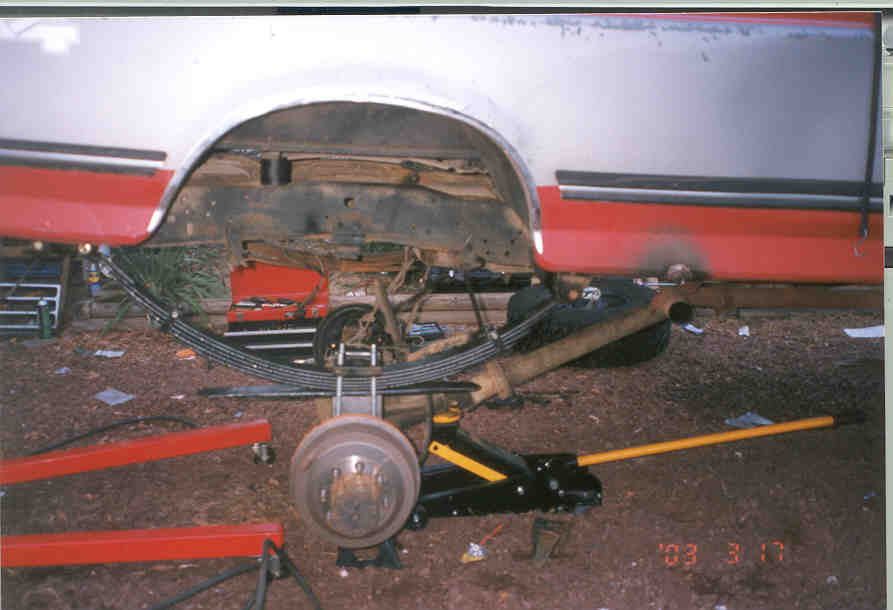 Rear leaf springs and drum brake of a white and red pickup with the wheel removed