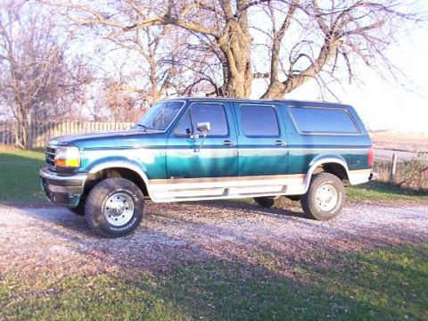 1995 Ford C-350 (Centurion Conversions) - This SUV with a camper shell is parked outdoors on a gravel surface.