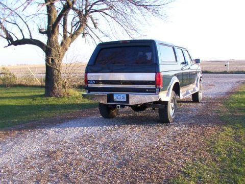 1995 Ford C-350 (Centurion Conversions) - A dark green Ford Bronco is parked on a gravel driveway next to a tree.