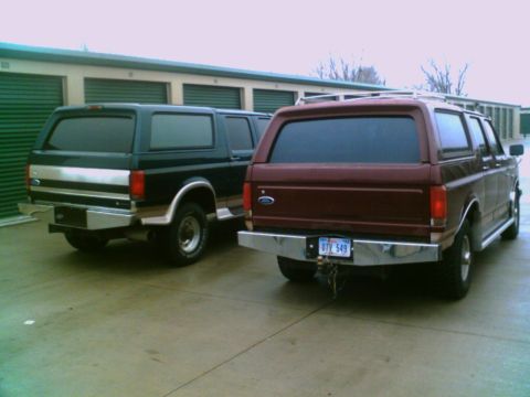 1995 Ford C-350 (Centurion Conversions) - Two Ford Bronco SUVs parked in front of storage units. One is black, the other is maroon.