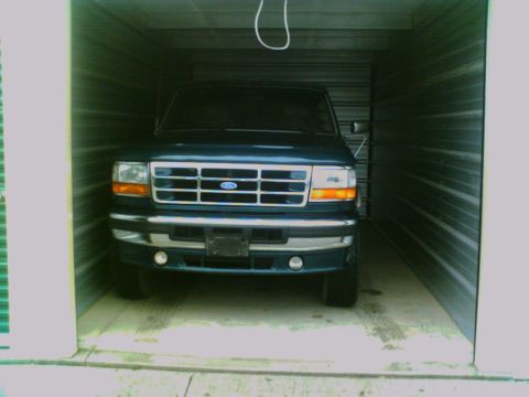 1995 Ford C-350 (Centurion Conversions) - A dark green Ford F-Series truck is parked inside a storage unit, facing forward.