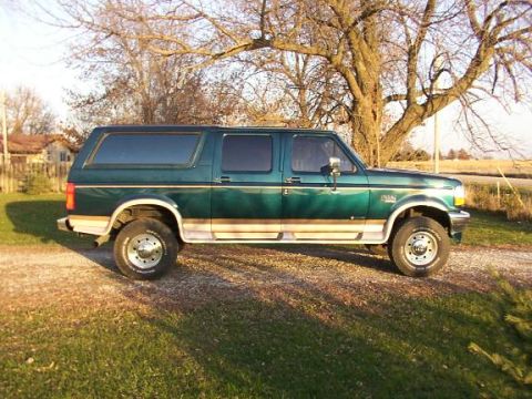 1995 Ford C-350 (Centurion Conversions) - Side view of a green extended cab pickup truck with a camper shell, parked outdoors.