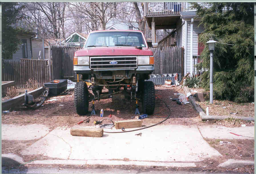 Red Ford pickup on jack stands with front bumper off, exposed lifted axle