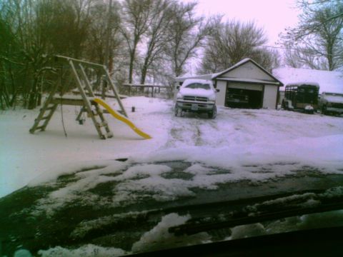 1995 Ford C-350 (Centurion Conversions) - A white pickup truck sits partially covered in snow in a driveway, with a garage and children's swing set visible.