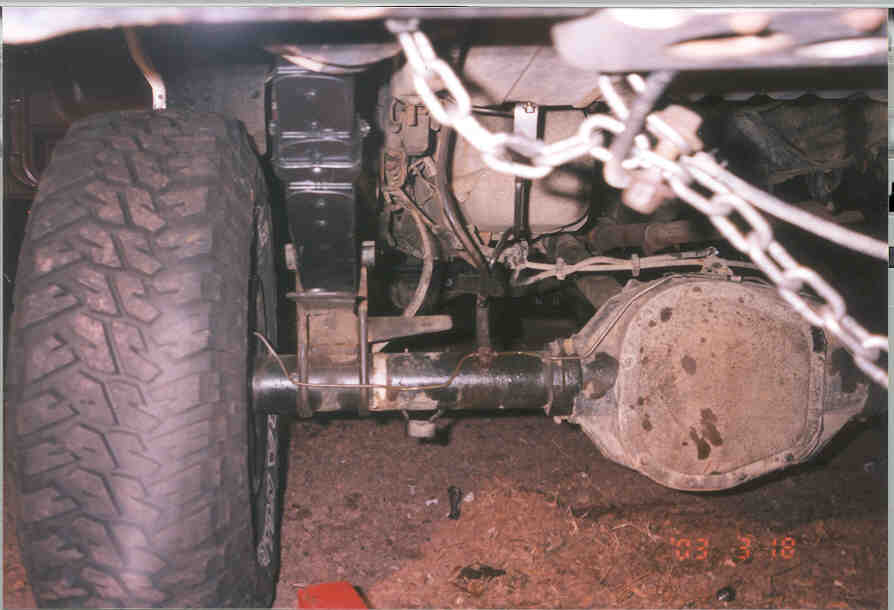 Underside view of a truck's solid front axle, differential, leaf spring and mud tire