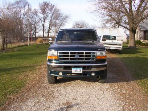 1995 Ford C-350 (Centurion Conversions) - A dark green pickup truck is parked on a gravel driveway in front of a house and trees.
