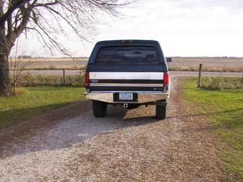 1995 Ford C-350 (Centurion Conversions) - Rear view of a Ford F-Series truck with a camper shell parked on a gravel driveway.