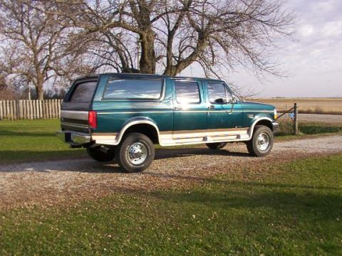 1995 Ford C-350 (Centurion Conversions) - This green extended cab pickup truck features a camper shell and is seen parked on a gravel driveway with a rural background.