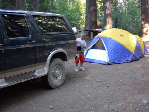 1995 Ford C-350 (Centurion Conversions) - A campsite scene with a vehicle and a tent set up in a wooded area.