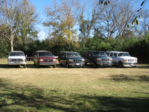 1995 Ford C-350 (Centurion Conversions) - Several Ford Broncos and an F-Series truck are parked on a lawn under a clear blue sky.