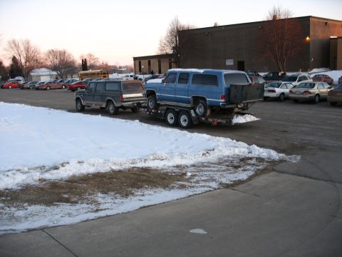 1995 Ford C-350 (Centurion Conversions) - A blue SUV is being towed by a dark SUV in a snowy parking lot with other cars visible.