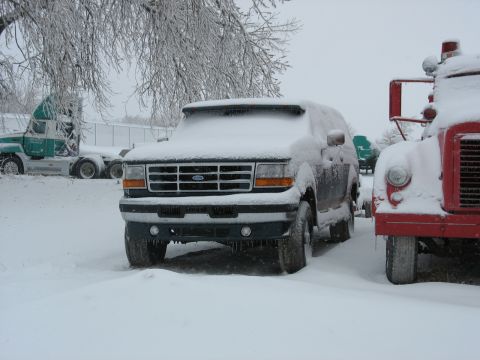 1995 Ford C-350 (Centurion Conversions) - A snow-covered Ford Bronco sits parked in a lot with other vehicles during winter weather.