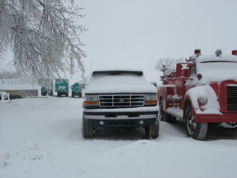 1995 Ford C-350 (Centurion Conversions) - Two vehicles, a Ford F-Series truck and a fire truck, are covered in snow during a winter scene.