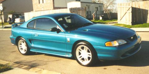 1994 Ford Mustang - A teal 1994 Ford Mustang GT coupe is parked on a residential street.