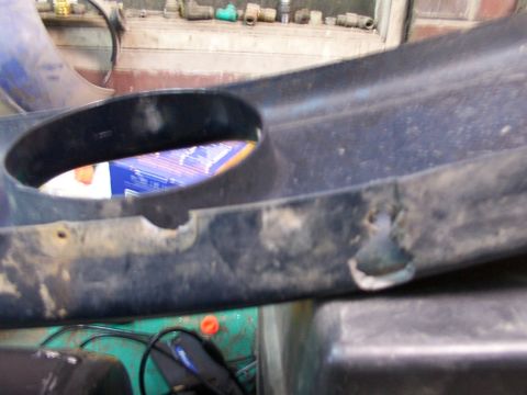 1995 Ford C-350 (Centurion Conversions) - Close-up of a black plastic automotive part, likely a front valance, showing a circular opening and some damage.