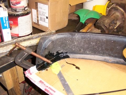 1995 Ford C-350 (Centurion Conversions) - A close-up view of a damaged automotive part being repaired with adhesive and a clamp.