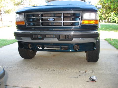 1995 Ford C-350 (Centurion Conversions) - Front view of a Ford truck, focusing on the bumper and grille. Some small parts are scattered on the concrete below.