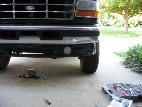 1995 Ford C-350 (Centurion Conversions) - Front view of a Ford truck, showing the grille, bumper, and a fog light, with tools laid out on the concrete.