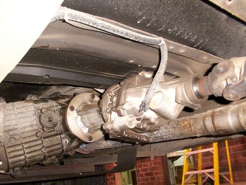 1995 Ford C-350 (Centurion Conversions) - Close-up of vehicle drivetrain parts, including transmission and driveshaft, with visible exhaust pipe.