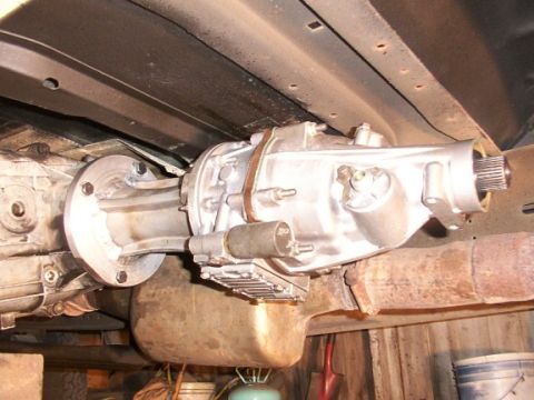 1995 Ford C-350 (Centurion Conversions) - Underside view of a silver auxiliary transmission or overdrive unit bolted to a larger transmission, with exhaust pipe visible.