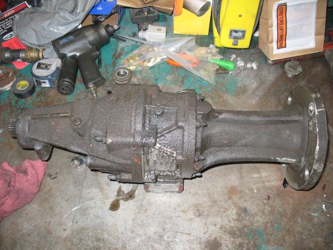 1995 Ford C-350 (Centurion Conversions) - A greasy transmission part sits on a cluttered workbench next to tools and other automotive supplies.