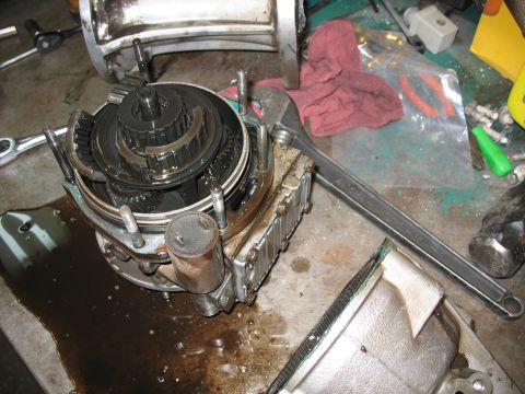 1995 Ford C-350 (Centurion Conversions) - A close-up view of a disassembled transmission part, showing internal gears and components on a cluttered workbench.