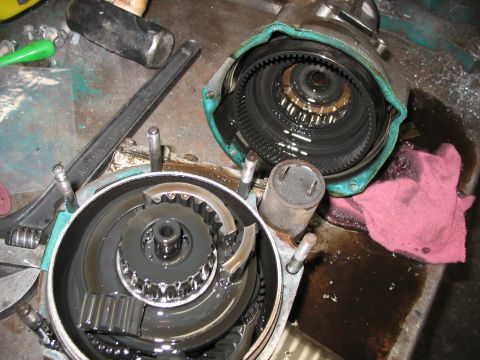 1995 Ford C-350 (Centurion Conversions) - A disassembled transmission part, showing internal gears and components submerged in dark fluid, with tools nearby.