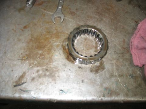 1995 Ford C-350 (Centurion Conversions) - A metal gear part with internal teeth rests on a stained workbench, accompanied by a wrench and a pink cloth.