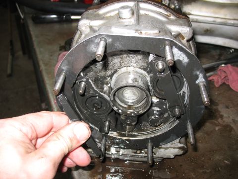 1995 Ford C-350 (Centurion Conversions) - A mechanic's hand holds a metal plate against a disassembled transmission part covered in grease.
