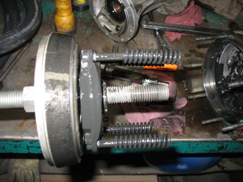 1995 Ford C-350 (Centurion Conversions) - Close-up of a disassembled brake drum assembly, showing springs and threaded components on a cluttered workbench.