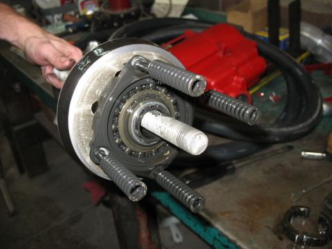 1995 Ford C-350 (Centurion Conversions) - A mechanic's hand holds a complex vehicle component springs and a bearing assembly on a cluttered workbench.