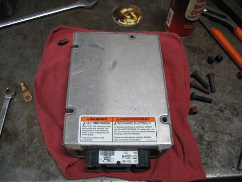 1995 Ford C-350 (Centurion Conversions) - Ford electronic control module with warning labels and connector, resting on a red cloth with tools nearby.