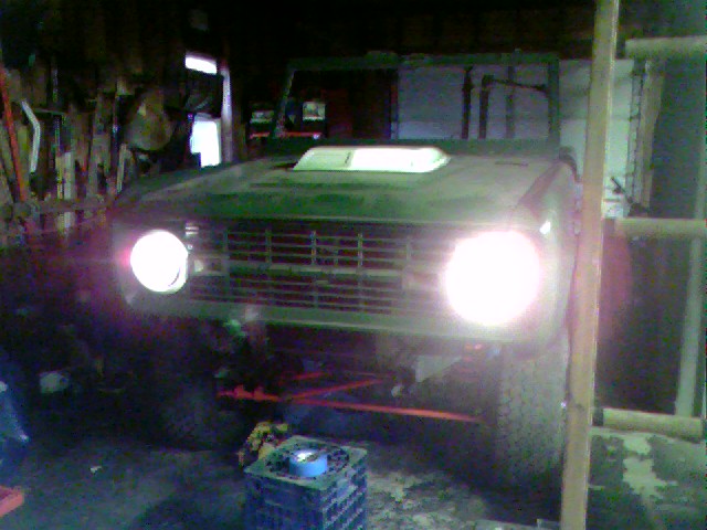 Green SUV with a hood scoop, front grille, and bright headlights, seen from the front