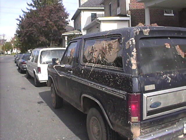 Black Ford Bronco with mud-splattered windows, parked on a street
