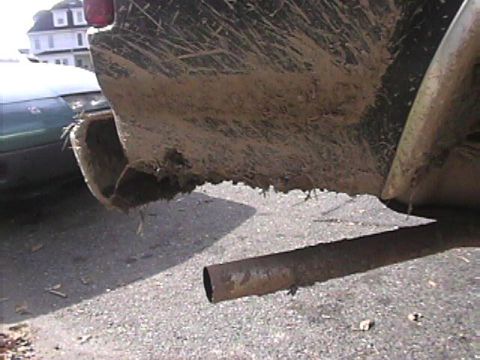 1985 Ford Bronco - Muddy rear bumper and exhaust pipe of a vehicle, with another car partially visible in the background.