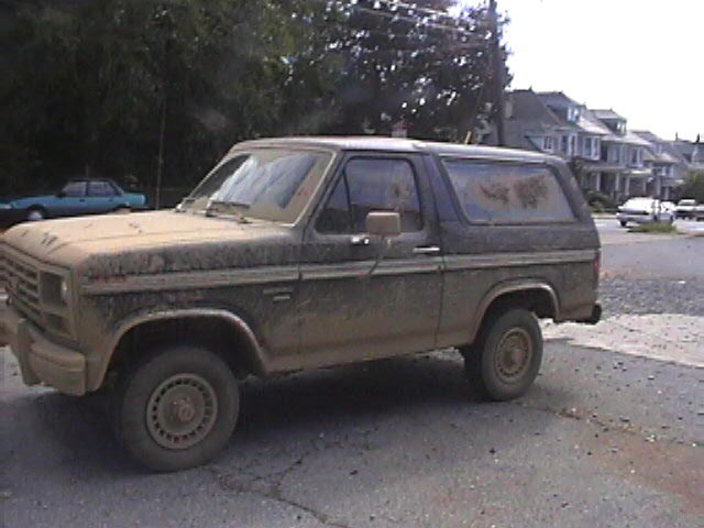 Mud-covered Ford Bronco parked on a street, side view