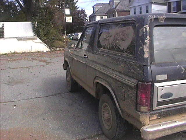 Mud-covered 1980s Ford Bronco, rear quarter view. Rear window is dirty