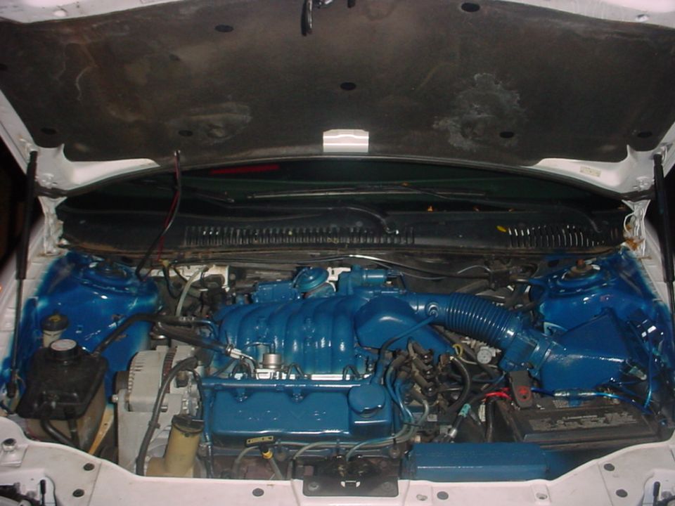 Engine bay of a white car with V6 engine and intake components painted bright blue
