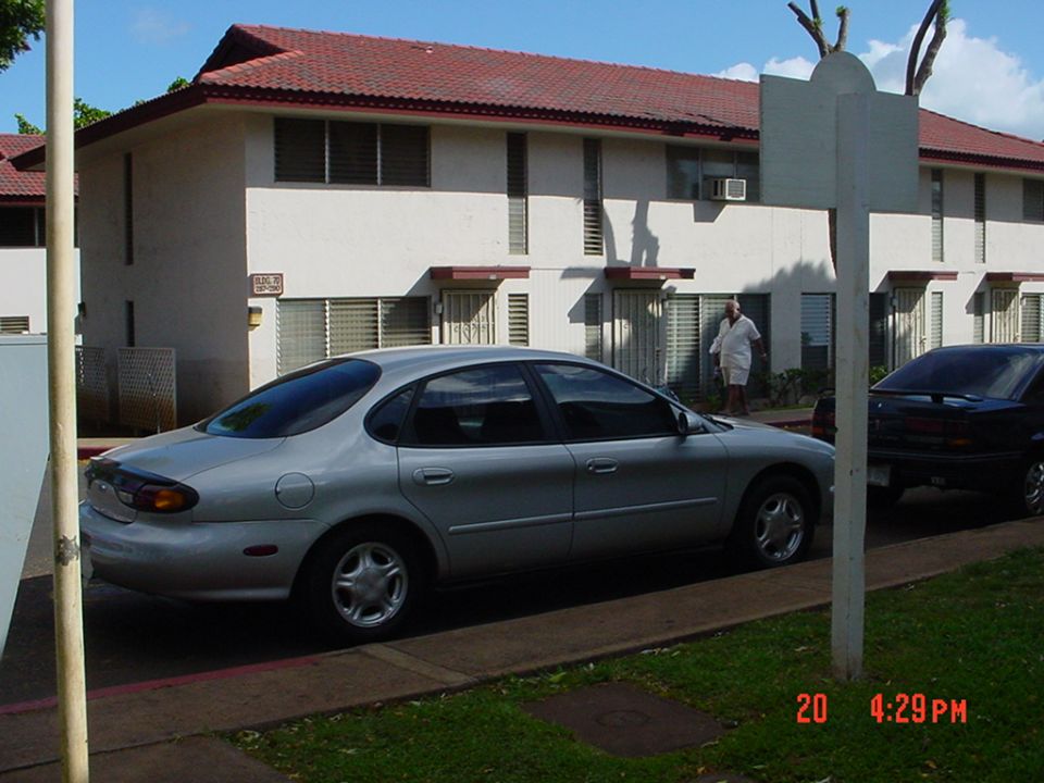 Silver Ford Taurus sedan parked beside two-story apartment, man standing nearby
