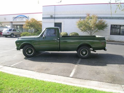 1996 Ford Bronco - This GMC pickup truck is parked in a lot next to a building with trees and bushes.