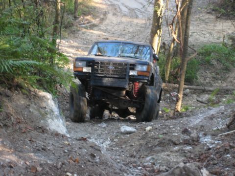 1989 Ford Bronco - Modified black Ford Bronco navigates a challenging off-road course with steep inclines and loose terrain.