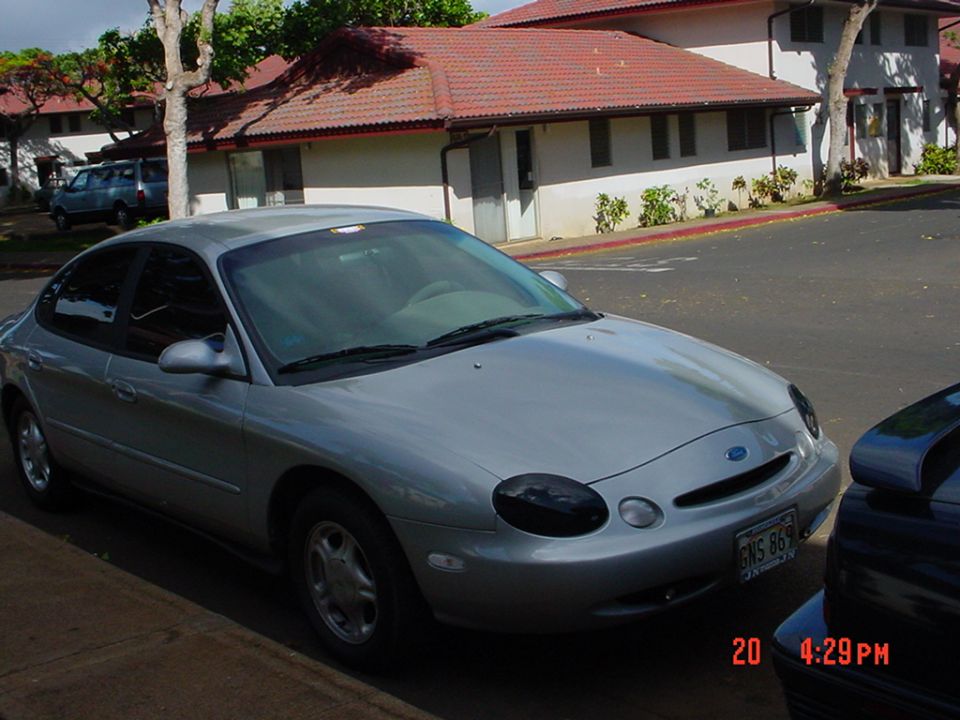 Silver Ford Taurus front three-quarter parked in apartment lot, oval grille emblem