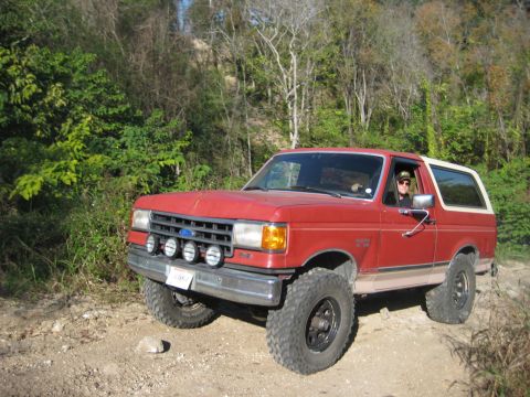1989 Ford Bronco - A red Ford Bronco with a white top is shown off-road.