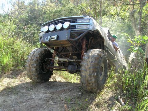 1989 Ford Bronco - This heavily modified truck, likely from the late 1980s, navigates a challenging off-road trail.