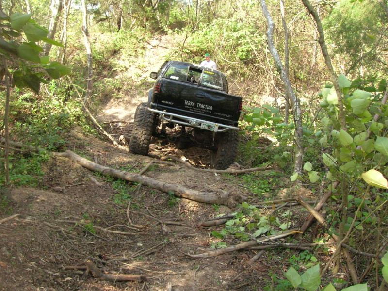 Black pickup truck with large tires navigating a wooded trail. Text on tailgate reads 'TERRA TRACTION CHEVROLET'