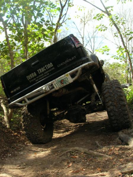 1989 Ford Bronco - A modified Chevrolet pickup truck navigates a challenging off-road trail through a wooded area.